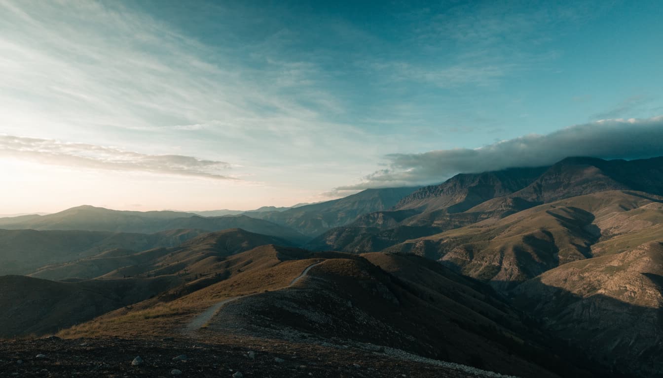 A quiet mountain ridge with a narrow path under a vast morning sky.